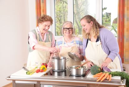 Zwei ältere Frauen kochen mit einer weiblichen Pflegekraft